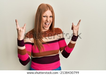 Young irish woman wearing casual clothes shouting with crazy expression doing rock symbol with hands up. music star. heavy concept. 