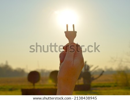 Woman holds a plug between thumb and forefinger facing the sun suggest clean energy supply 