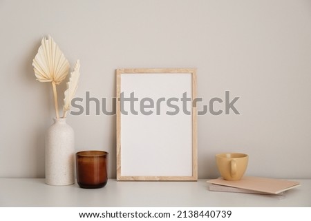 Nordic style home office desk in living room. Picture frame mockup, candle, dry flowers in vase, cup of tea, paper notebook on white table.