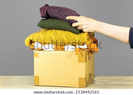 closeup woman putting shirt in carton box with used clothes for donation, collection and support of war victims, helping people, charity