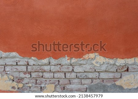 Wall texture with red plaster and peeling bottom with exposed brick. Wall background with red plaster and brick with cement. Ideal for background with copy space Royalty-Free Stock Photo #2138457979