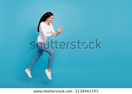 Full length body size view of attractive cheerful active girl jumping using device blog isolated on bright blue color background