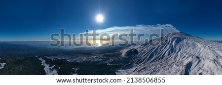 180 degree aerial photo of Etna in winter at dawn. Snow-covered craters, Etna in activity, Valle del Bove and summit craters. Snowy woods. South-East, North-East, Voragione, Bocca Nuova. Sartorius.