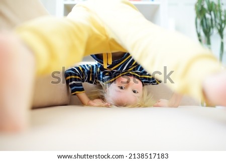 Little boy is standing on own head on sofa at home. Bored lonely child. Difficulties of family with preschool children during working at home. Mischievous baby. Royalty-Free Stock Photo #2138517183