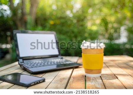 coffee cup paper with a Computer laptop and phone in green nature background. Work remotely or from home. soft focus.shallow focus effect.