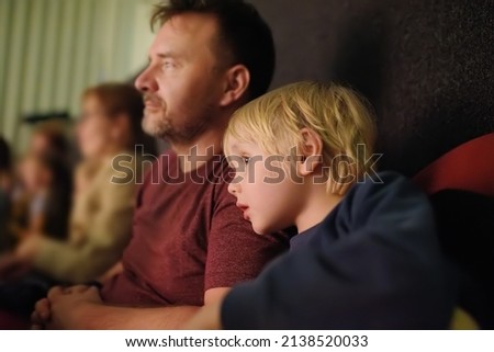 Cute little boy with his father watching cartoon movie in the cinema or performance in viewer hall of theatre. Leisure entertainment for family with kids. Cultural event for children.
