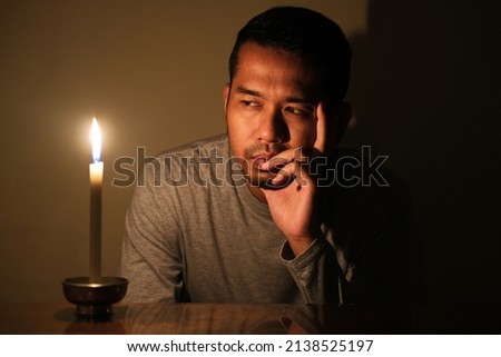 Adult Asian man looking to the burning candle with sad expression during electricity power failure Royalty-Free Stock Photo #2138525197