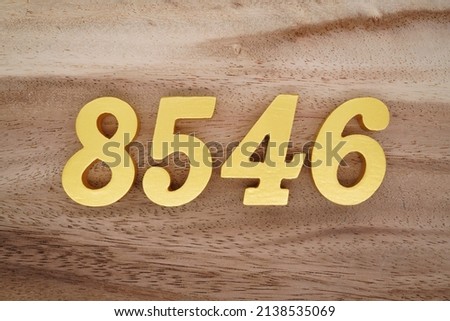 Wooden  numerals 8546 painted in gold on a dark brown and white patterned plank background.