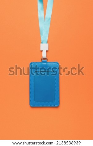 A blue badge with a ribbon on a bright orange background. Name badge. A device for cards and business cards. Flat lay.