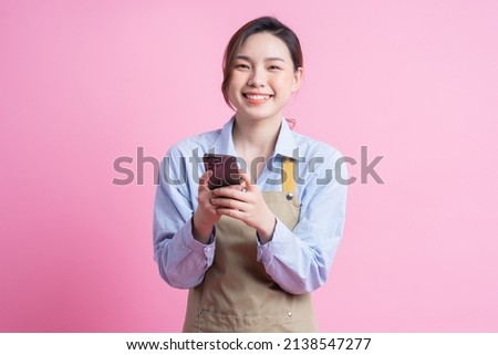 Young Asian waitress standing on pink background Royalty-Free Stock Photo #2138547277
