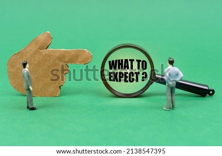 Business and finance concept. On the green surface there is a figure of a hand, miniature figures of people and a magnifying glass with the inscription - What To Expect