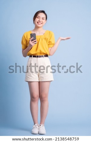 Full length image of young Asian woman using smartphone on blue background