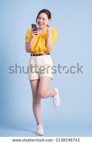 Full length image of young Asian woman using smartphone on blue background Royalty-Free Stock Photo #2138548761