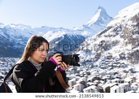 Traveler photographer woman with camera taking pictures of landscape of Swiss Alps on sunny winter day ..