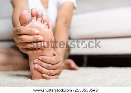 Foot pain, Asian woman feeling pain in her foot at home, female suffering from feet ache use hand massage relax muscle from soles in home interior, Healthcare problems and podiatry medical concept Royalty-Free Stock Photo #2138558543
