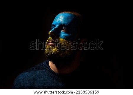 Stop war, conflict between Ukraine and Russia. Portrait of a young man with his face painted in the blue and yellow colors of the flag. looking left