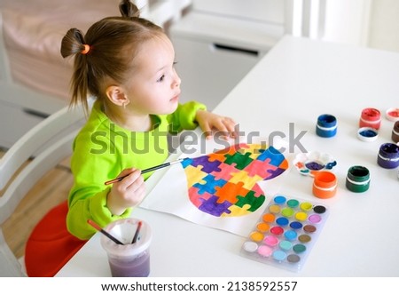 The child looks forward in surprise with bulging eyes. Profile of a astonished girl drawing a postcard for Autism Day with a picture of puzzles. ASD