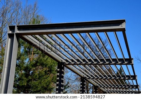 metal construction of the bus stop, gazebo pergola shelter. The roof is designed for climbing plants. L-painted beams and L-shaped ribs shading blinds with stripes on promenade in the park, sky,  blue Royalty-Free Stock Photo #2138594827