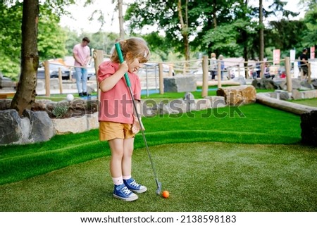 Cute preschool girl playing mini golf with family. Happy toddler child having fun with outdoor activity. Summer sport for children and adults, outdoors. Family vacations or resort. Royalty-Free Stock Photo #2138598183