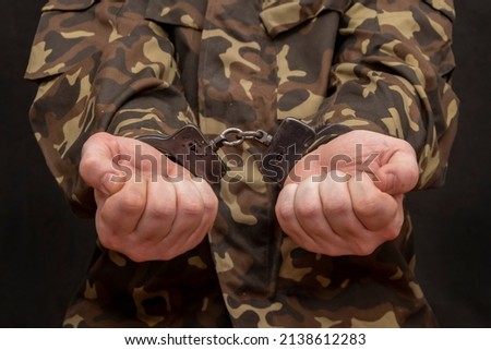 A military man in camouflage is handcuffed on a dark background. Concept: war criminal, prisoner of war, tribunal for deserters, traitor to the motherland 1.