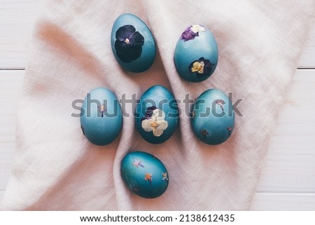 Naturally dyed cyan blue pressed flower Easter eggs on neutral beige tablecloth background. Top view, flat lay style. Handmade craft natural decoration.