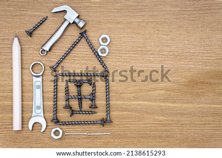 House outline made from screws, hand tools, nuts and nails on a wooden background with copy space. Home renovation tips and tricks concept.