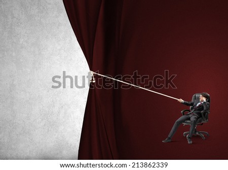 Young businessman sitting in chair and pulling curtain with rope