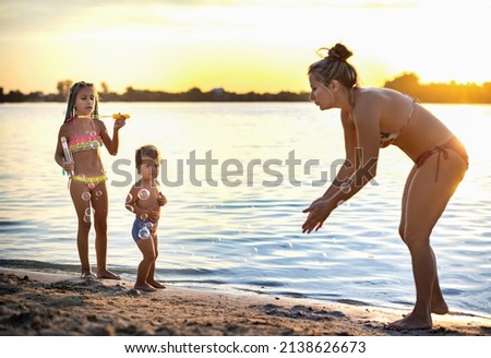 Brother and sister play with their mom blowing bubbles on the lake