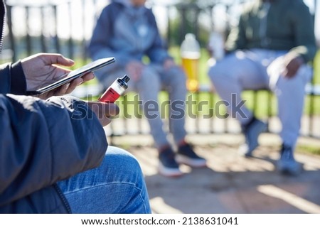 Close Up Of Teenagers With Mobile Phone Vaping and Drinking Alcohol In Park Royalty-Free Stock Photo #2138631041