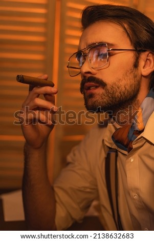 young man with mustache and eyeglasses smoking cigar