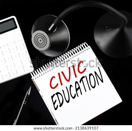 Opened paper notebook with text CIVIC EDUCATION with a pen, calculator and table lamp on a black background.