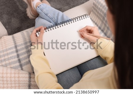 Young woman drawing in sketchbook on sofa, above view