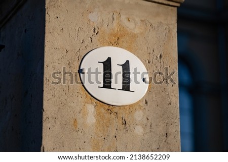 Number eleven on a plate on a wall. House number 11 on the exterior of a building. Part of an address in a residential district. Entrance of a home outside from the street.