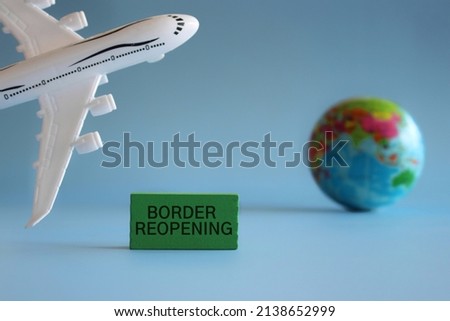 Wooden cube with text BORDER REOPENING, toy plane and earth globe. Travel and transportation concept