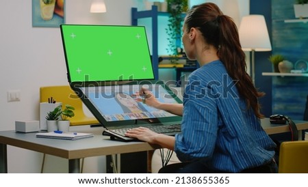 Woman with horizontal green screen editing photos on touch screen monitor. Photographer working with retouching app, having chroma key for isolated background and mockup template
