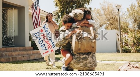 Patriotic soldier being welcomed by his family at home. American serviceman embracing his children after returning home from the army. Military man reuniting with his wife and children. Royalty-Free Stock Photo #2138665491