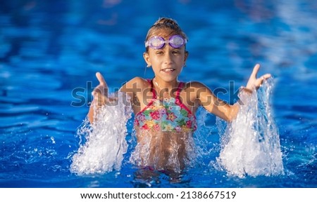 A little girl in a bright pink swimsuit with transparent black goggles for swimming, straightens her goggles and then dives into a deep blue pool with a chimta of clear water