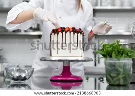 Pastry chef decorates the cake with chocolate levels of berries and mint. Royalty-Free Stock Photo #2138668905