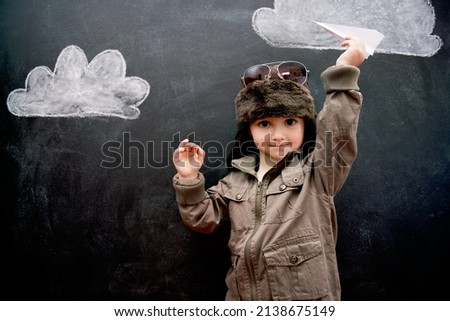 With education, anything is possible. A little boy playing with an airplane in front of clouds drawn on a blackboard.