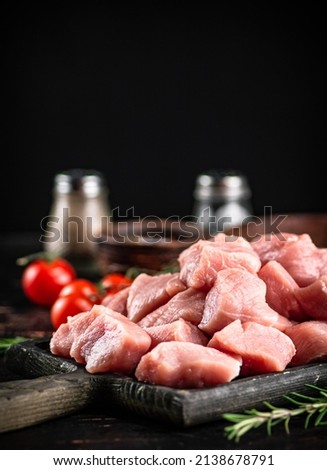 Pieces of raw pork on a cutting board with spices, tomatoes and rosemary. On a rustic dark background. High quality photo