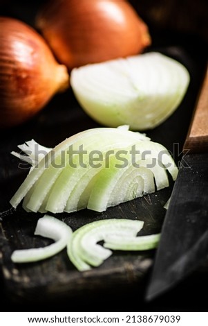 Pieces of onion on a cutting board with a knife. On a wooden background. High quality photo