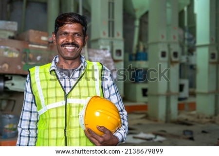 Portrait of happy smiling industrial worer with safety helmet in hand looking at with copy space - concept of safety measures, skilled labour and workforce. Royalty-Free Stock Photo #2138679899