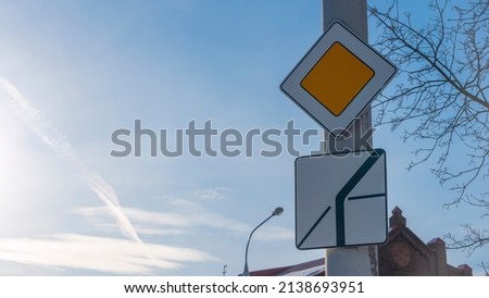 Road sign main road in sun beams against blue sky with clouds. Priority road sign on the background of sky and old building. Road rules concepts.