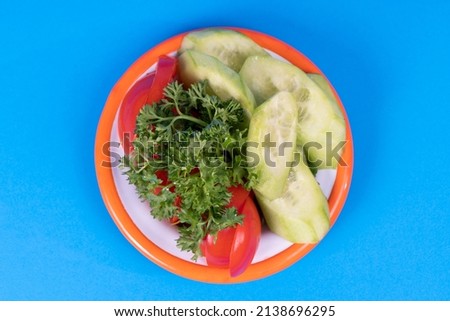 Cropped view of plate of delicious salad shot from top angle with selective focus on isolated setting on blue background. Image of diced cucumbers, diced tomatoes and parsley.