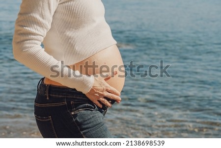 Silhouette of pregnant young woman sunbathing in front of the sea.