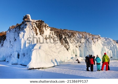 Frozen Lake Baikal on sunny February day. Group of tourists travels on the ice of Small Sea and photographs beautiful coastal ice-covered rocks of Olkhon Island. Winter travel and adventure concept