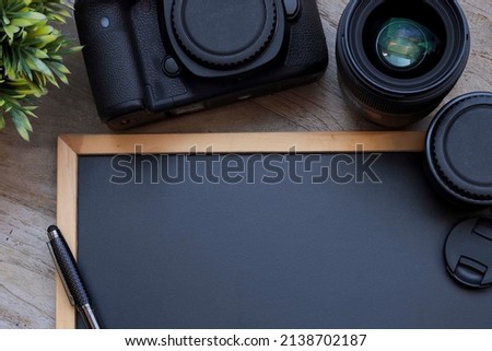 Partially empty black chalkboard with pen, lenses and camera on the wooden table. Education and business concept, Noise is visible due to the texture of the subjects