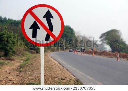 Traffic road sign with symbols of arrows to warn drivers do not overtake that can cause car accidents beside the rural road.                          