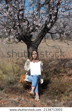 Young woman looking at camera sitting on a tree with flowers