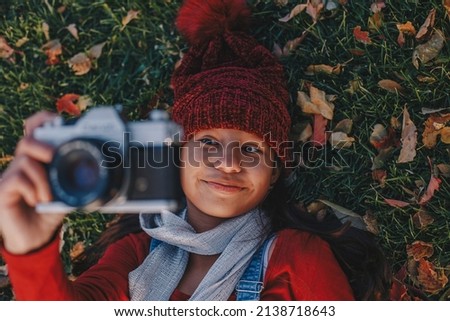 Young girl wearing a red beanie laying in the ground taking photos with a film camera 